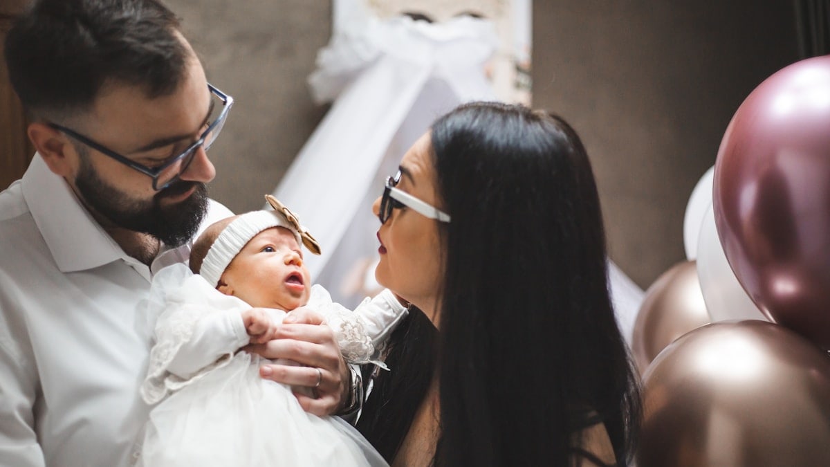 Mother and father holding their young baby girl, and looking at her.